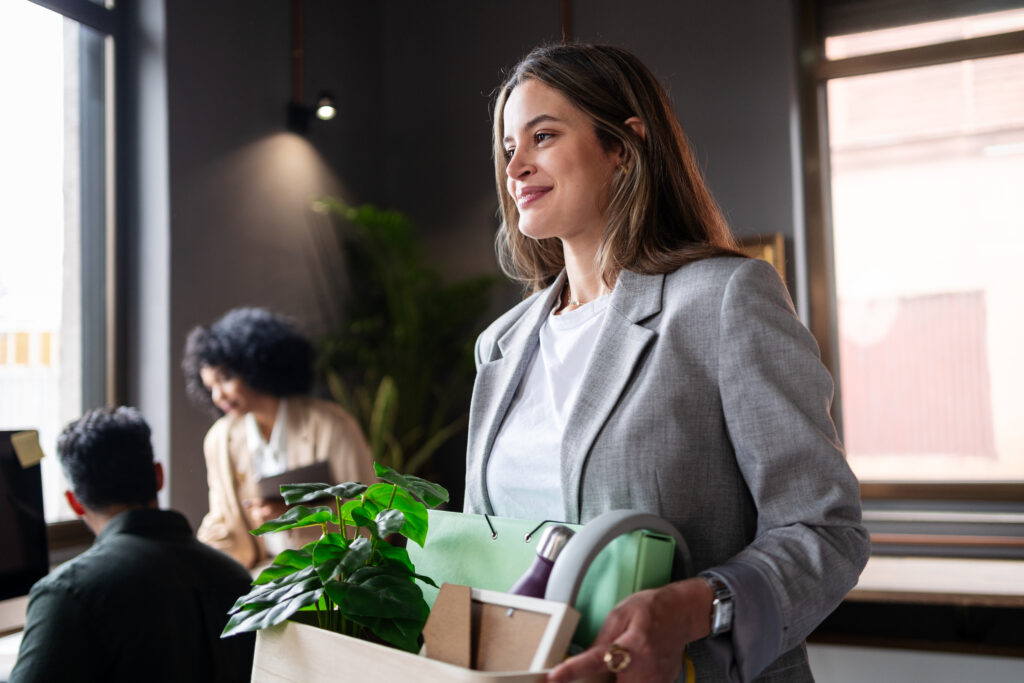 Eine professionelle Managerin verlässt ihren Arbeitsplatz, hält einen Karton mit persönlichen Gegenständen in der Hand und lächelt selbstsicher, nachdem sie ihre aktuelle Position gekündigt hat. Eine professionelle Managerin verlässt ihren Arbeitsplatz, hält einen Karton mit persönlichen Gegenständen in der Hand und lächelt selbstsicher, nachdem sie ihre aktuelle Position gekündigt hat.